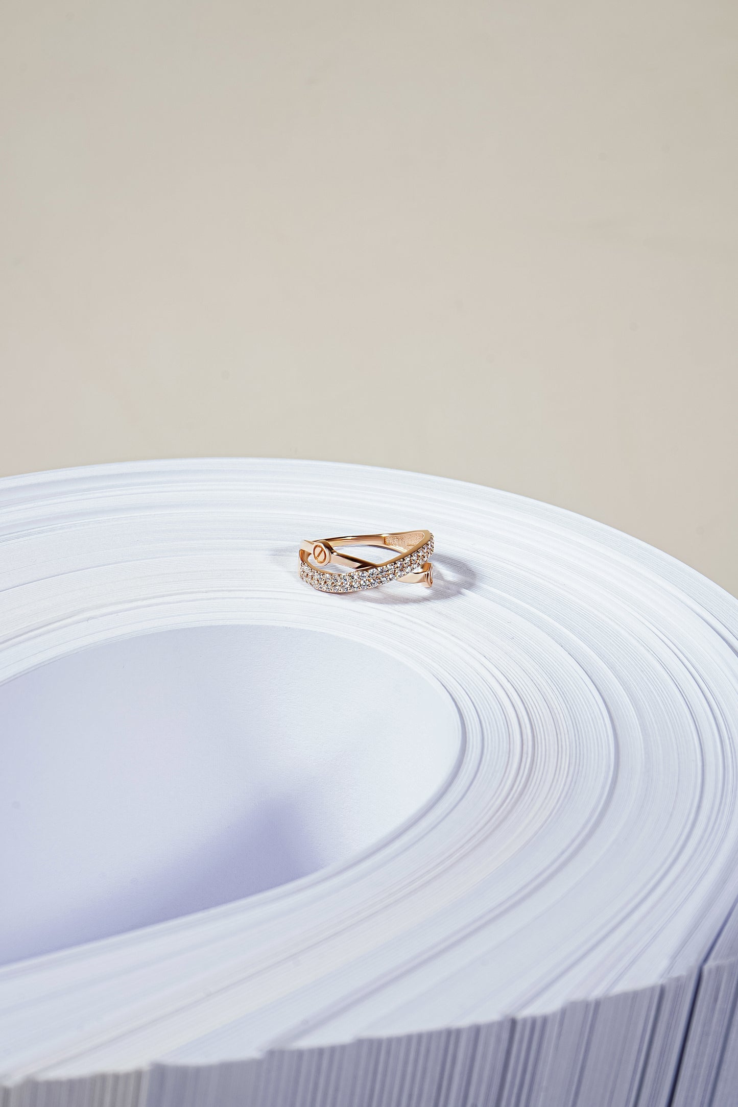 Каблучка з червоного золота, яка складаєтся з двох перехрещених полос, верхня з фіанітами в два ряди. Зображена на широкій зігнутій стопці білого паперу.