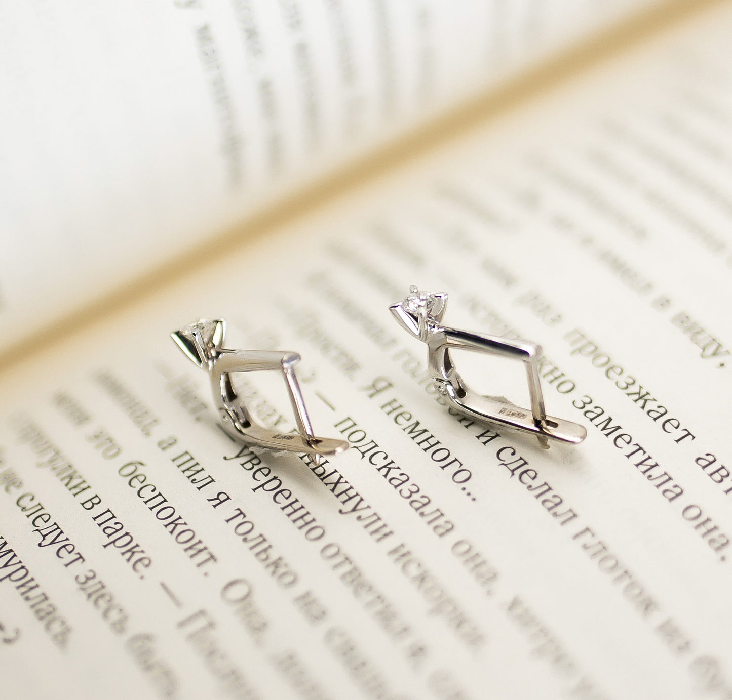 Сережки з білого золота з діамантом таанглійською застібкою. Зображені на фоні сторінок книги