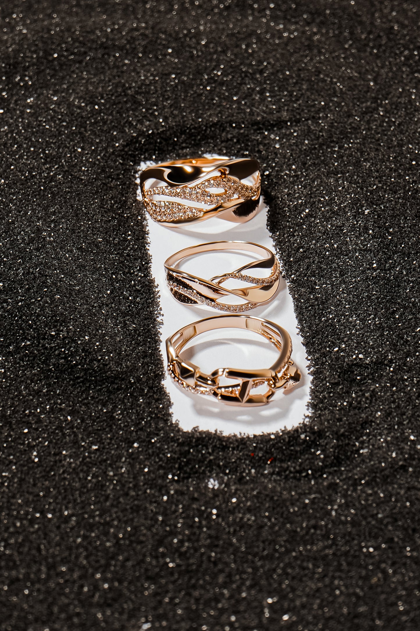 Три каблучки з червоного золота на сірому піску