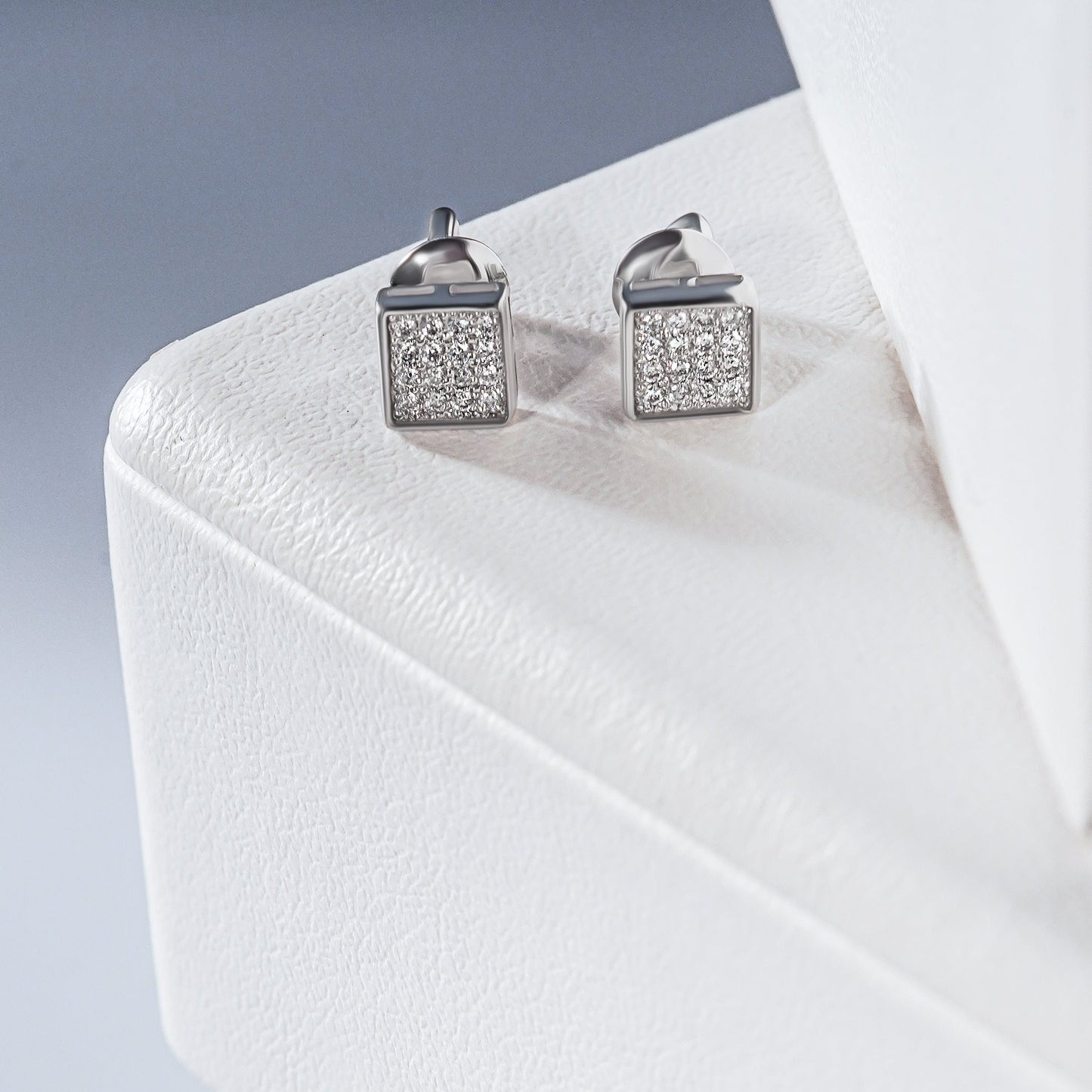 Дві пари сережок з білого золота з діамантами. Мають квадратну та круглу форму. Зображені на білих підставках