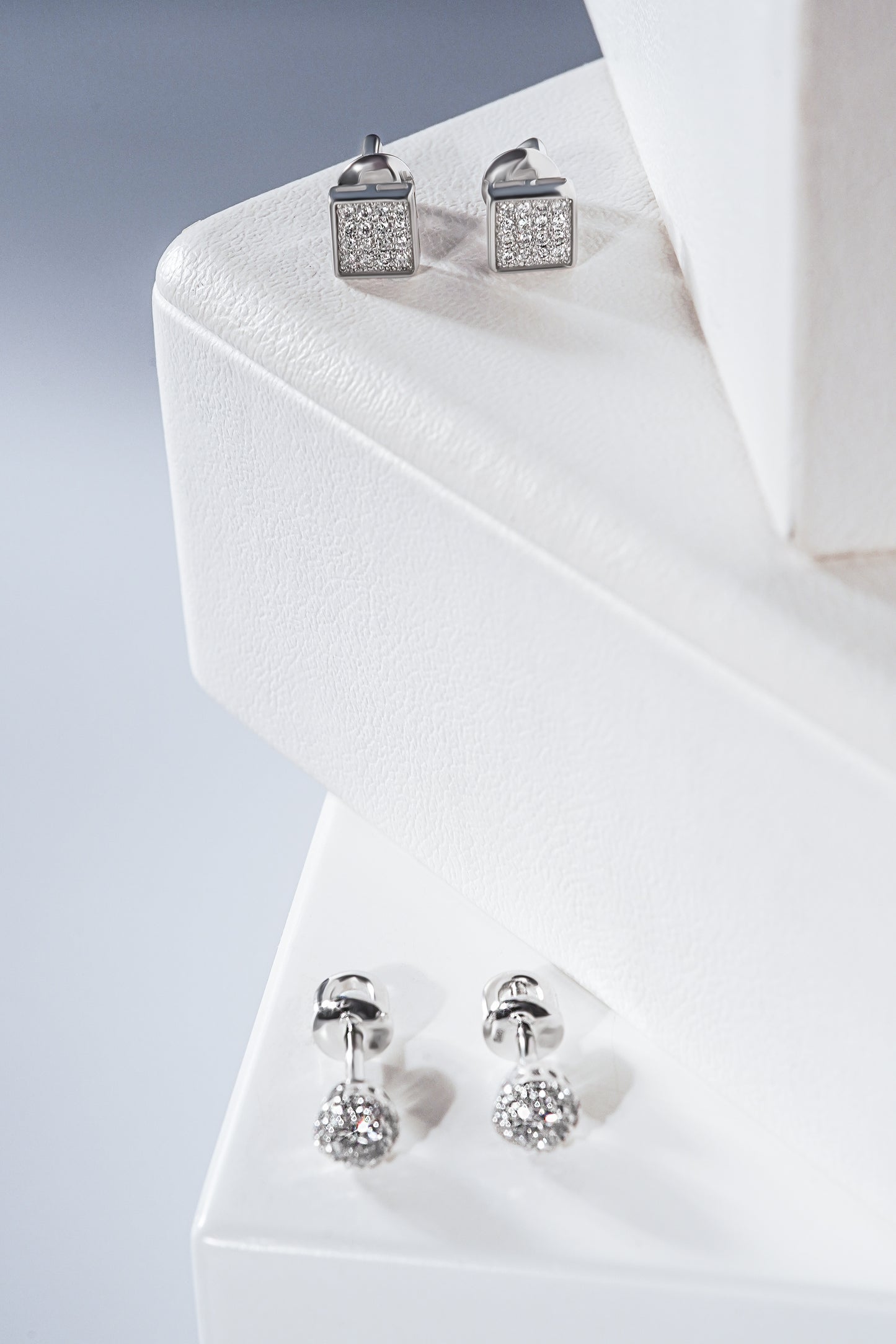 Дві пари сережок пусетів з білого золота круглої та квадратної форми. Зображені на білих підставках