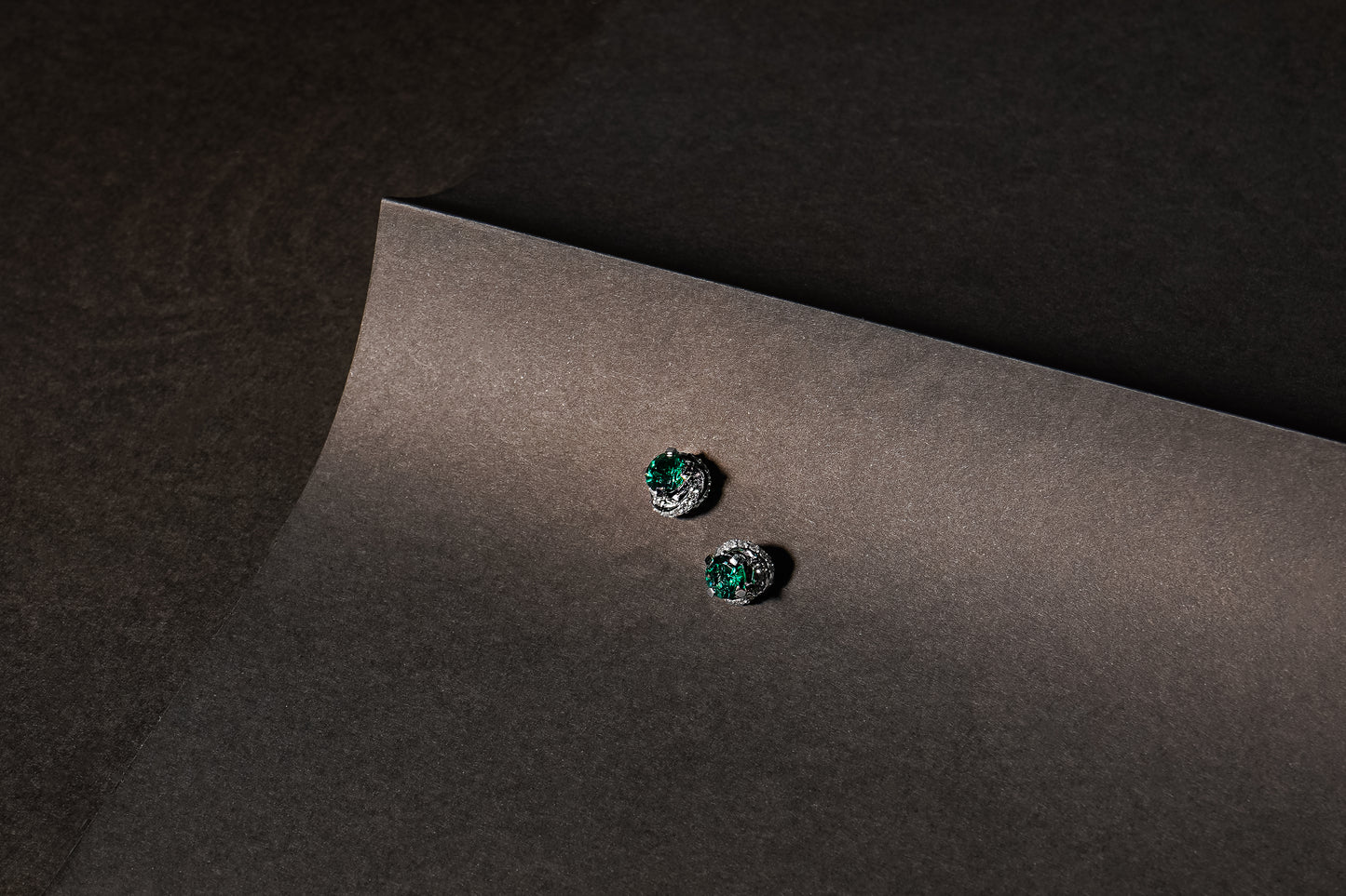 Сережки пусетиз білого золота зі смарагдом та діамантами та чорному аркуші паперу