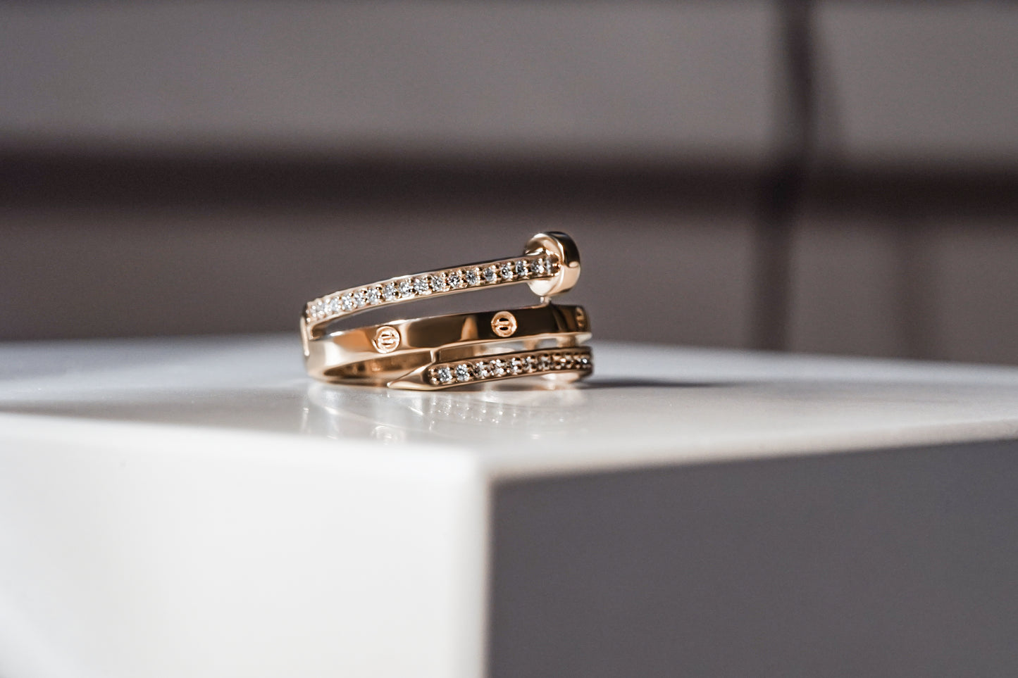 Каблучка з червоного золота Cartier з діамантами на сірому фоні та на білій підставці