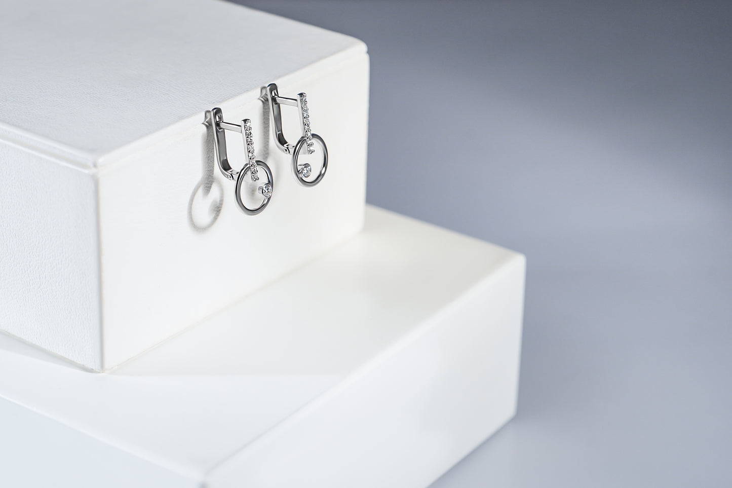 Сережки з білого золота з діамантами та англійською застібкою. З кругом внизу сережки. Зображені на білій підставці