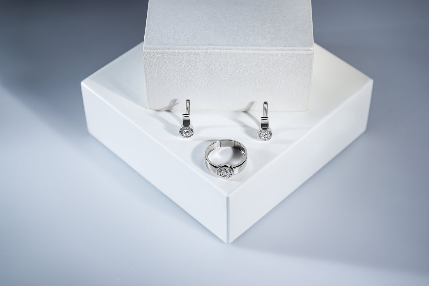 Сережки та каблучка з білого золота з діамантами з англійською застібкою. Зображені на білій підставці