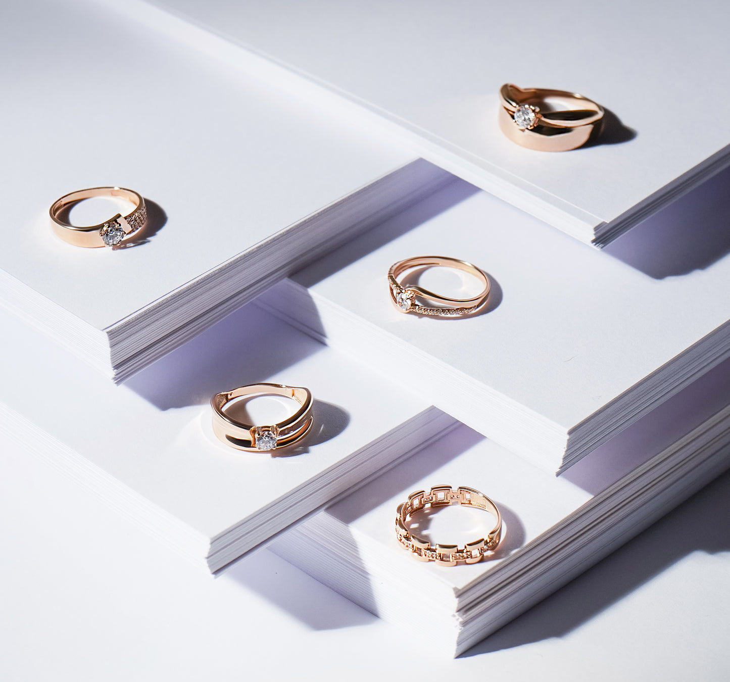П'ять різних каблучок з червоного золота зображені на підставках з паперу.