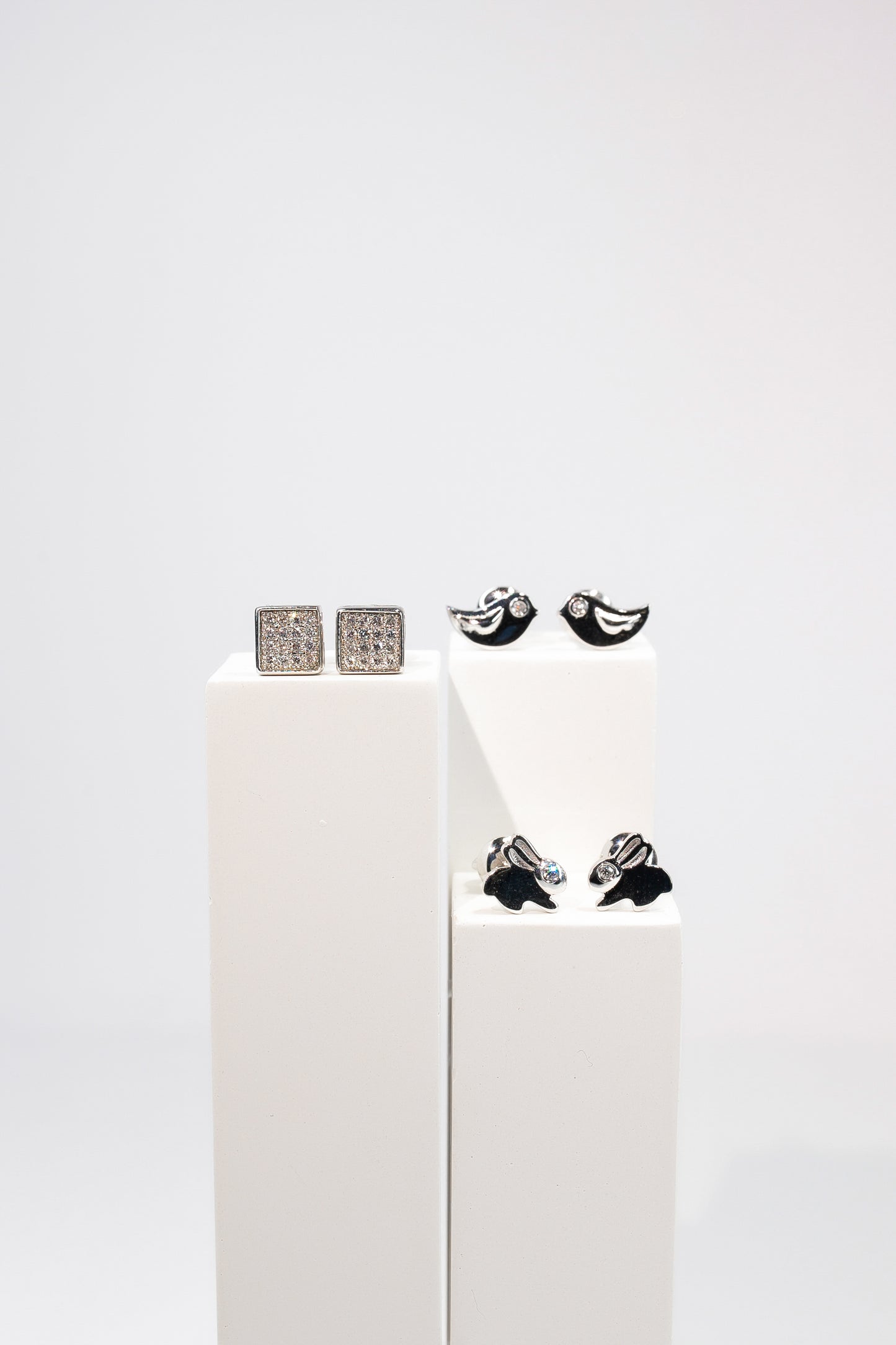 Три пари дитячих сережок пусетів діамантами на білій підставці . Мають квадратну форму, форму пташки та зайчика