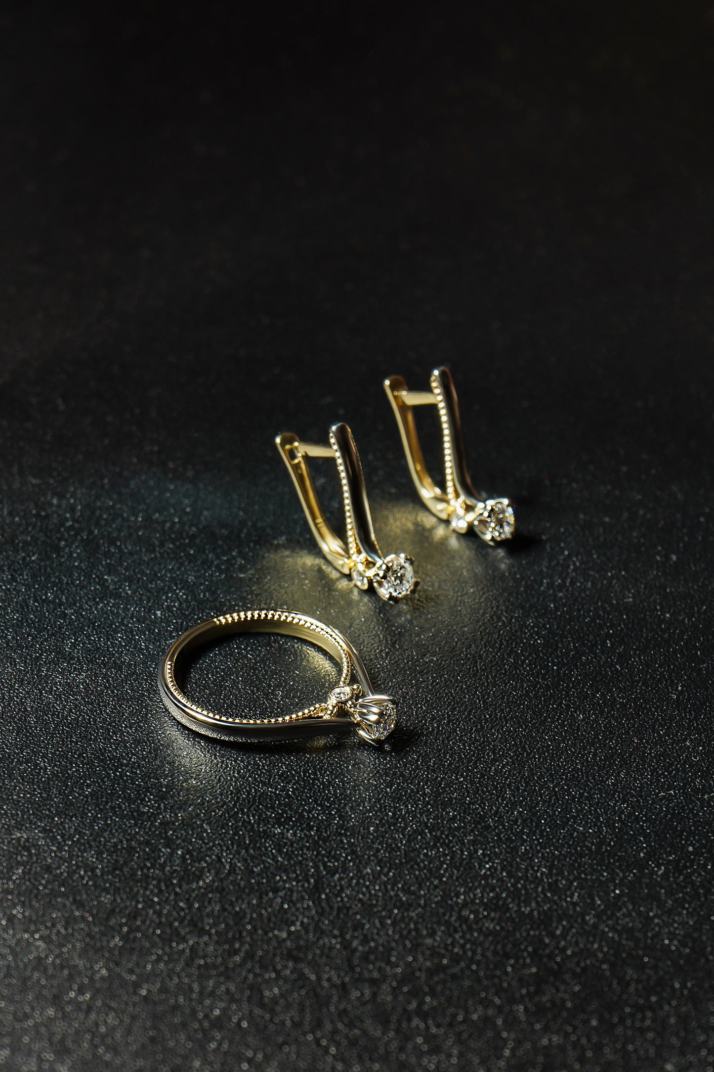 Набір каблучка та сережки з комбінованого золота з діамантом середнього розміру по центру. Зображений на чорному фоні
