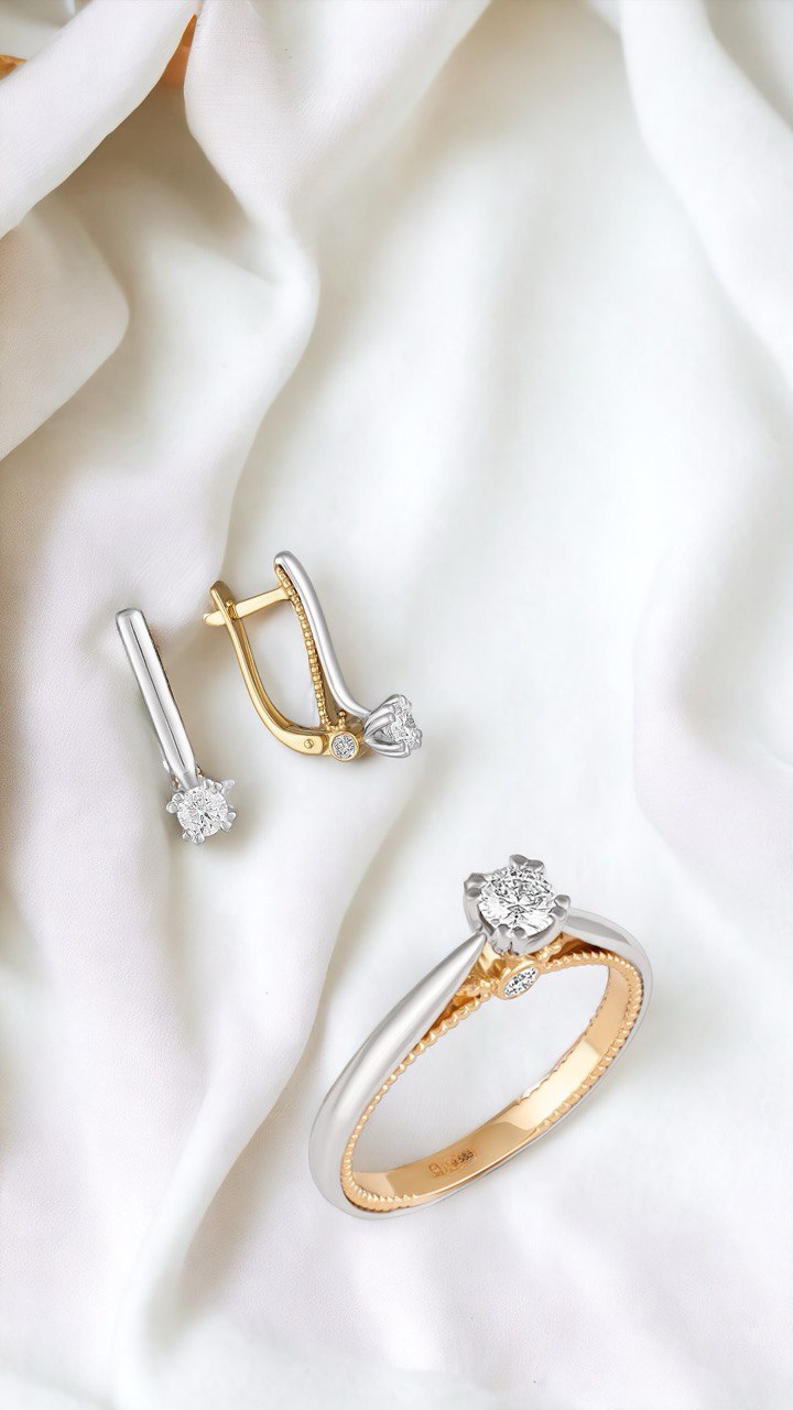 Набір каблучка та сережки з комбінованого золота з діамантом середнього розміру по центру. Зображений на білій, хвилястій тканині