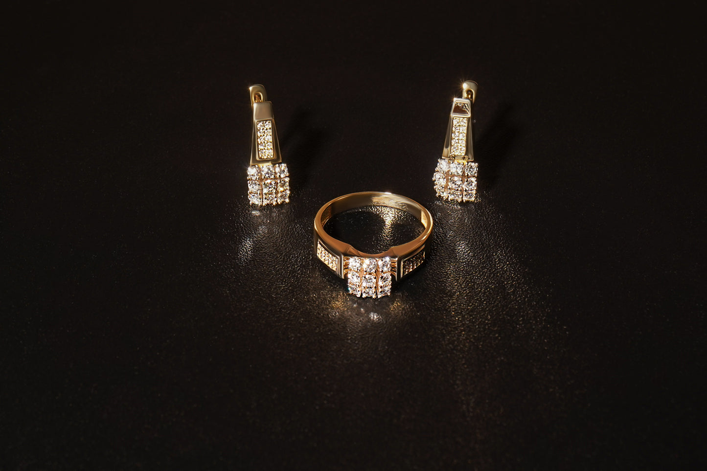 Набір сережки та каблучка з червоного золота з маленькими діамантами викладеними у формі квадрата. Зображений на чорному фоні