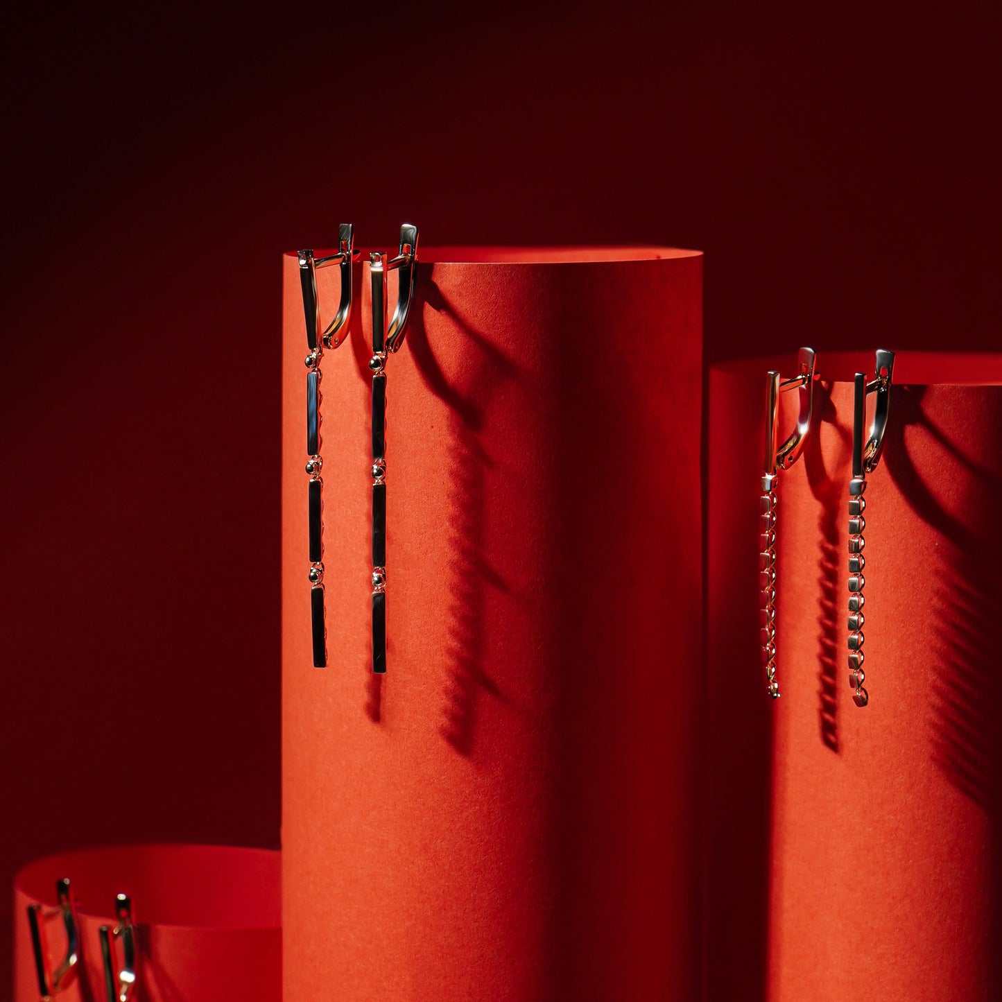 Три пари довгих сережок зображені на підставках червоного кольору
